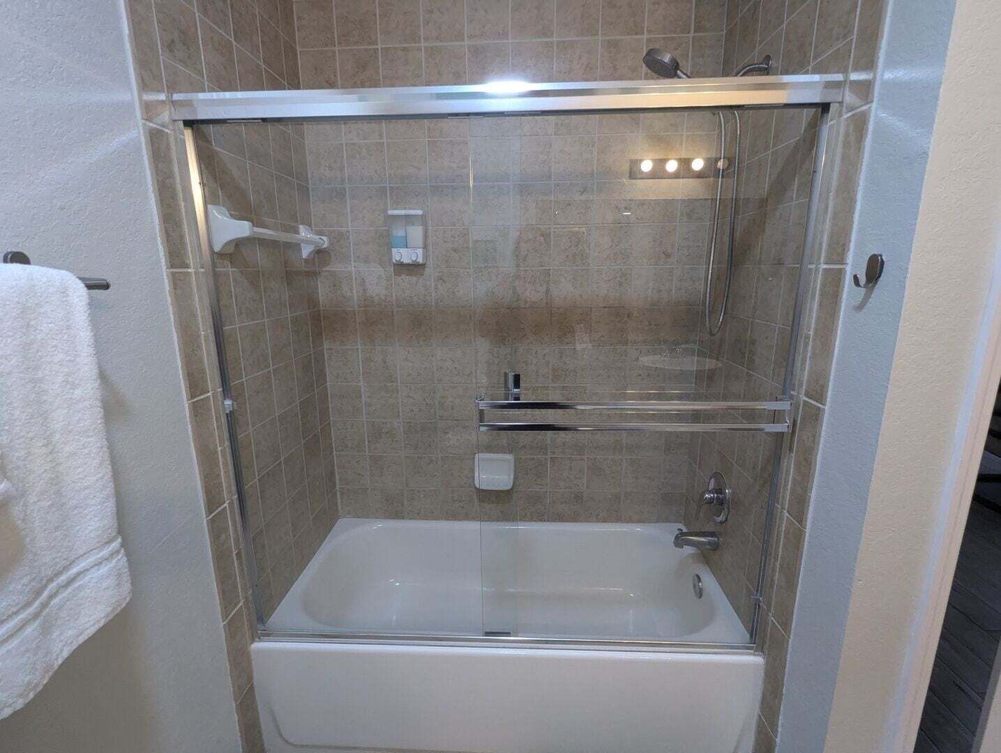 A walk-in shower with a glass door, a bathtub, and a towel rack.