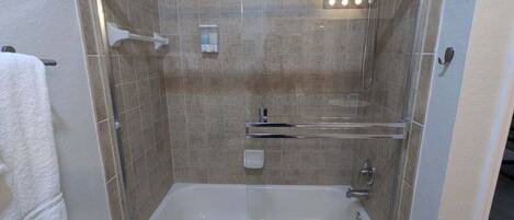 A walk-in shower with a glass door, a bathtub, and a towel rack.