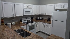 Una cocina con armarios blancos, estufa, microondas y refrigerador.