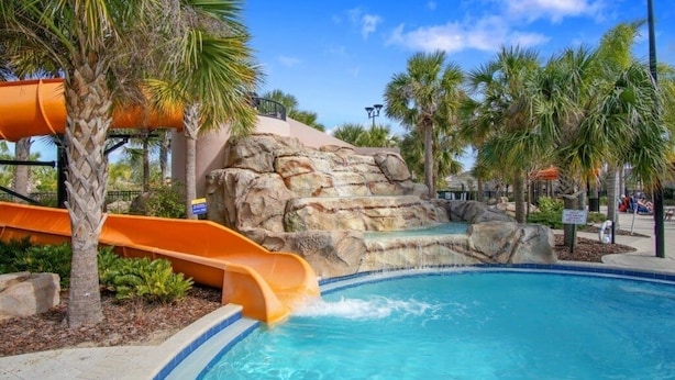 A pool area with a water slide, palm trees, and a rocky backdrop. - St5336ob Solterra Resort 5 Bedroom Home (Davenport)