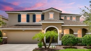 A two-story house with a garage, a covered driveway, and a landscaped front yard with palm trees and shrubs. - St5336ob Solterra Resort 5 Bedroom Home (Davenport)