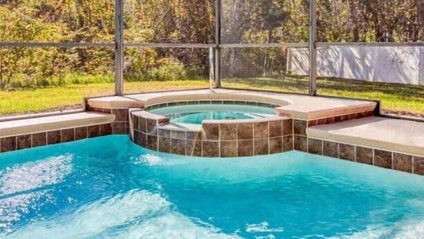 A swimming pool with a hot tub area, surrounded by a covered deck and a view of a landscaped garden. - Ws192tl Watersong 5 Bed Pool Home 5 Bedroom Home (Davenport)