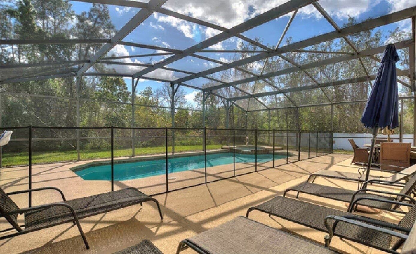 A covered outdoor area with a pool, lounge chairs, and a table with an umbrella.