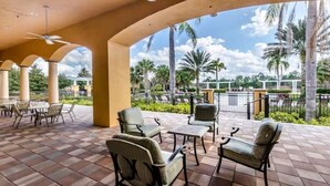 A covered outdoor seating area with chairs and tables, palm trees, and a view of a parking lot. - Ws192tl Watersong 5 Bed Pool Home 5 Bedroom Home (Davenport)