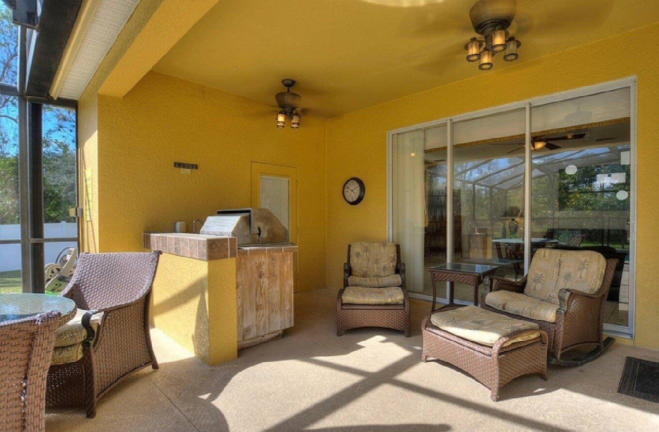 Un patio soleado con mobiliario de mimbre, una estación de parilla y grandes puertas de cristal que dan a un espacio al aire libre.