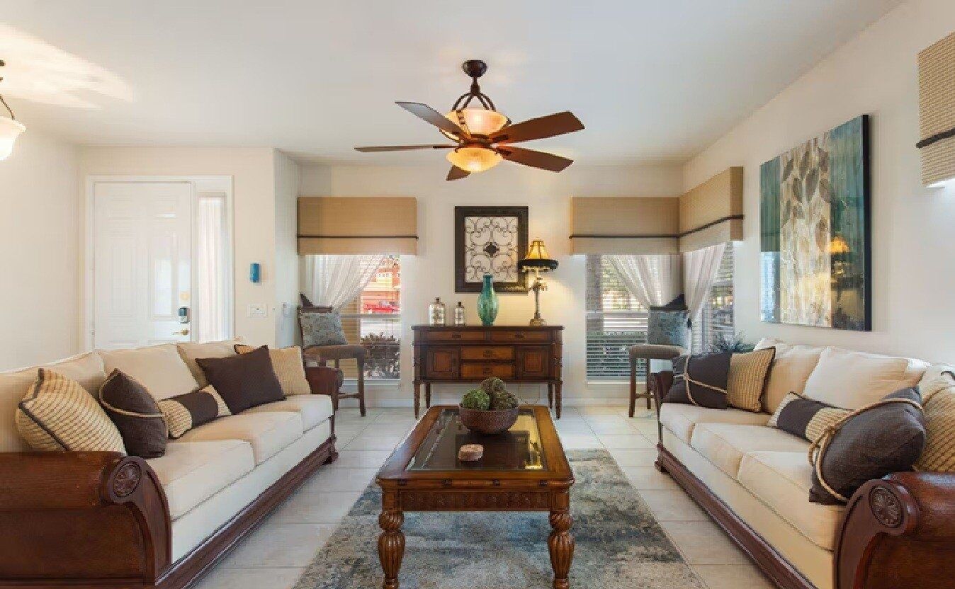 A living room with two sofas, a coffee table, a ceiling fan, and a dining area with a table and chairs.