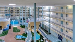 Un vestíbulo de hotel de varios niveles con una piscina central, varios balcones y una zona de juegos para niños.