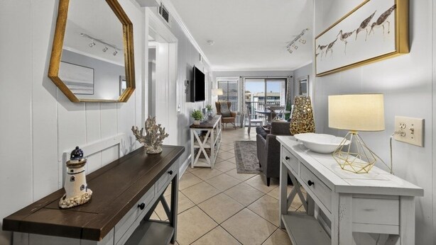 Una cocina moderna con armarios blancos, encimera de madera y un espejo grande. Se ve un comedor con mesa y sillas a través de una puerta abierta.