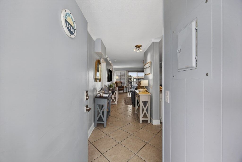 A hallway with a tiled floor, a door with a sign, and a view into a dining area with a table and chairs.