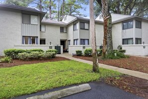 A row of three-story apartment buildings with numbered doors, a well-maintained lawn, and a tree in the foreground. - Harbour Master - Monthly Rates Through 2/28/26! 3 Bedroom Villa (Hilton Head Island)