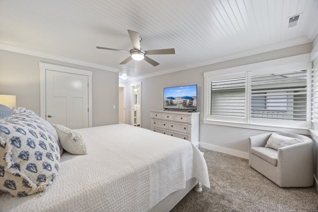 Quarto com cama, ventilador de teto, televisão, cômoda e janela com persianas.