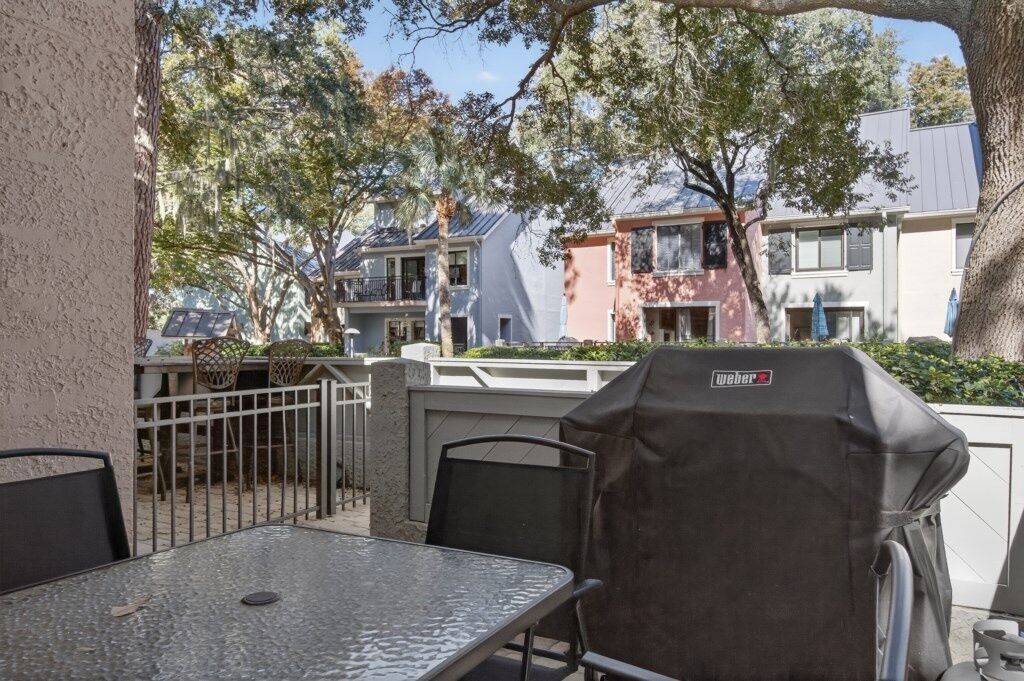 An outdoor patio with a table and chairs, a grill, and a view of neighboring houses.