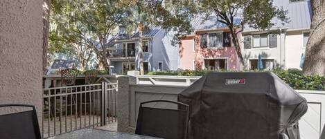 An outdoor patio with a table and chairs, a grill, and a view of neighboring houses.