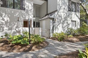 A modern building with a paved entrance, a gate, and a small garden area with various plants. - Sea Pines - 867 Ketch Court 2 Bedroom Home (Hilton Head Island)