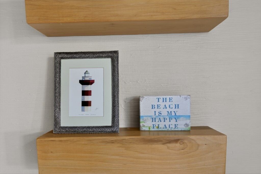 A framed picture of a lighthouse on a wooden shelf, next to a sign that reads "THE BEACH IS MY HAPPY PLACE."
