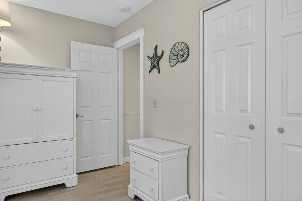 A bedroom with a large white wardrobe, a bedside table, and two doors.