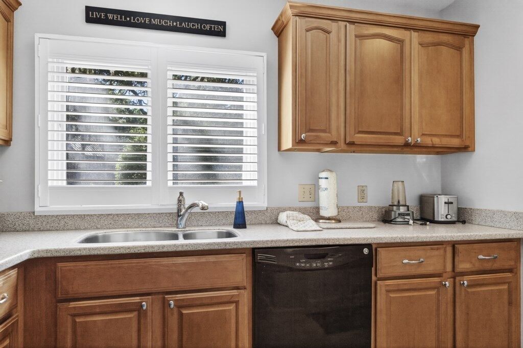A kitchen with wooden cabinets, a dishwasher, a sink, and a window with blinds.