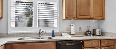 A kitchen with wooden cabinets, a dishwasher, a sink, and a window with blinds.