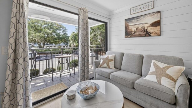 A living room with a grey sofa, starfish pillows, a bowl on a coffee table, and a painting labeled "BEACH" on the wall. - South End - 180 Sea Side Villas 1 Bedroom Condo (Hilton Head Island)