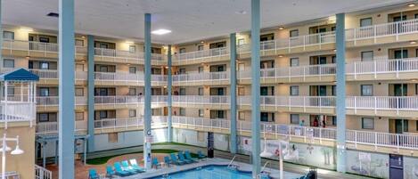A multi-story hotel with a central swimming pool surrounded by lounge chairs, balconies, and a small hot tub.