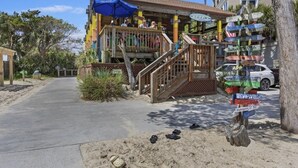 Un bâtiment situé au bord de la plage, doté d’une terrasse en bois et d’un escalier menant à une zone abritée.