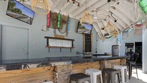 Un espace bar doté d’un comptoir en pierre, de tabourets en bois et de décorations suspendues.