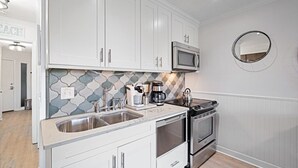 Una cocina moderna con gabinetes blancos, un lavamanos de acero inoxidable, un microondas, una estufa y una cafetera.