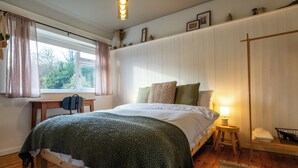 Una camera da letto con un letto, una scrivania, una sedia, una finestra con tende, un comodino con una lampada e un termosifone.
