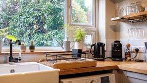 Una cucina con lavello, una macchina da caffè, una pianta e una finestra vista verde.