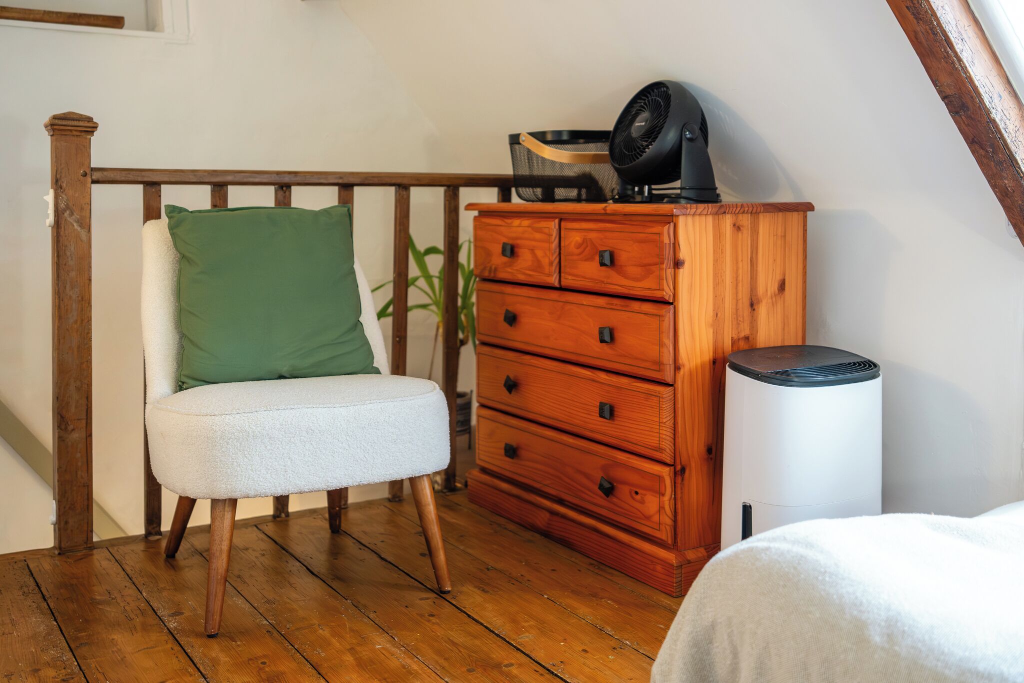 Una habitación con una silla de madera, un cojín verde, un aparador de madera y un cubo de basura blanco.