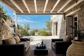 An outdoor patio with wicker furniture, a stone wall, and a view of the landscape. - Lux 9-bdrm professionally managed villa in Mykonos,private pool & sea views (Mikonos)