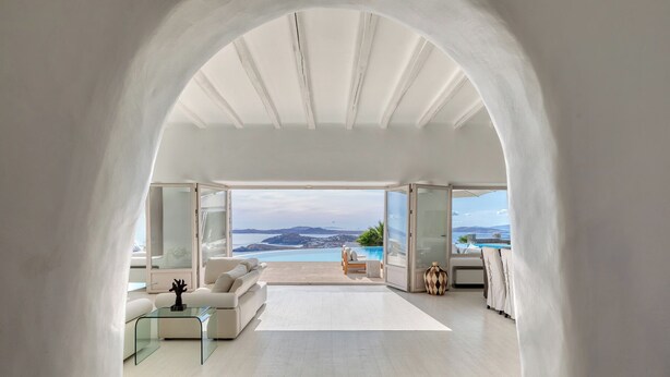Een moderne woonkamer met een grote boogvormige deuropening naar een balkon met uitzicht op een schilderachtig zeegezicht.