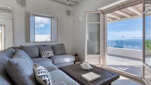 Een moderne woonkamer met een grijze modulaire bank, een houten salontafel en uitzicht op zee door een glazen deur.