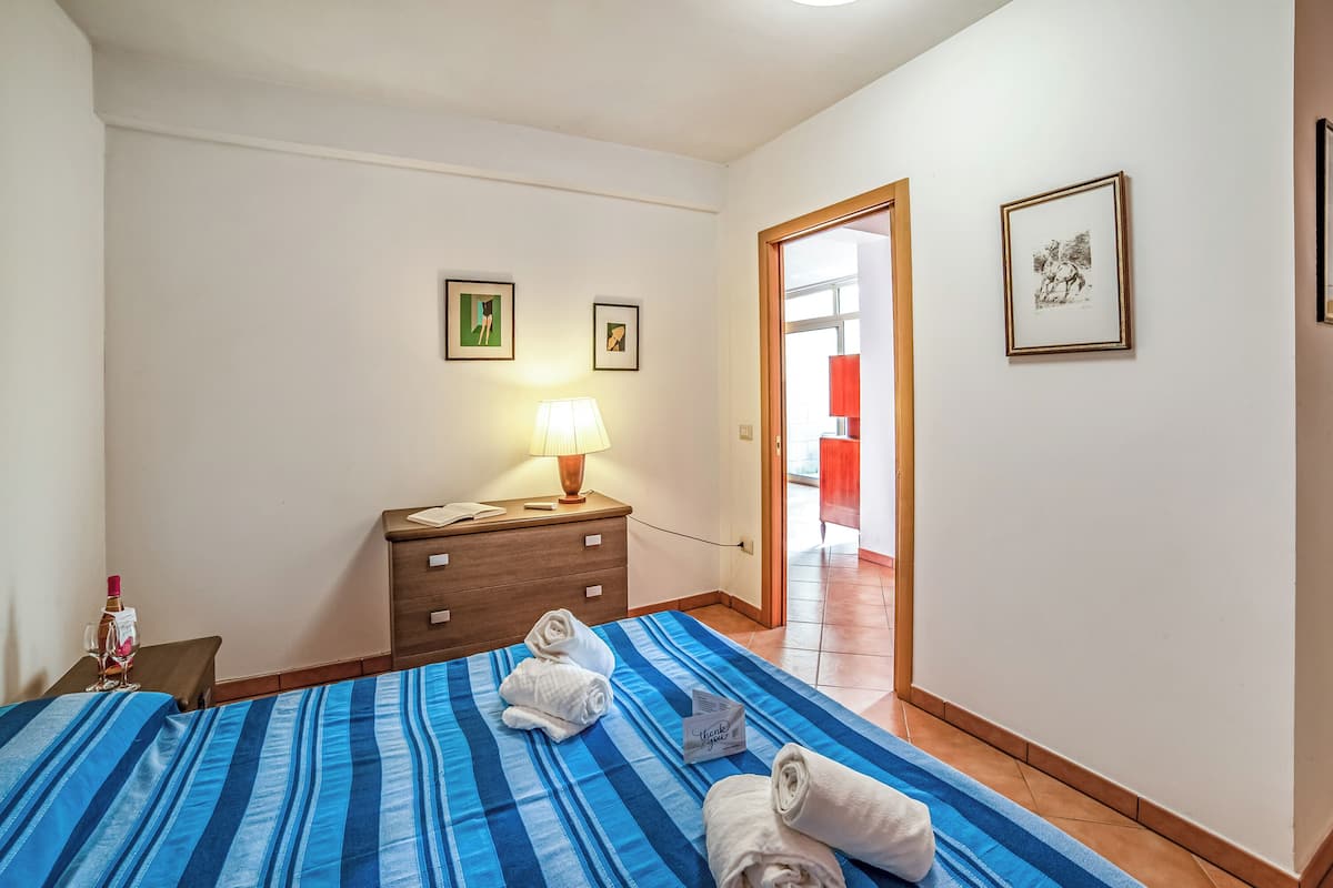 Ein Hotelzimmer mit einem Bett, einem Nachttisch mit Lampe, einer Holzkommode und zwei gerahmten Bildern an der Wand.