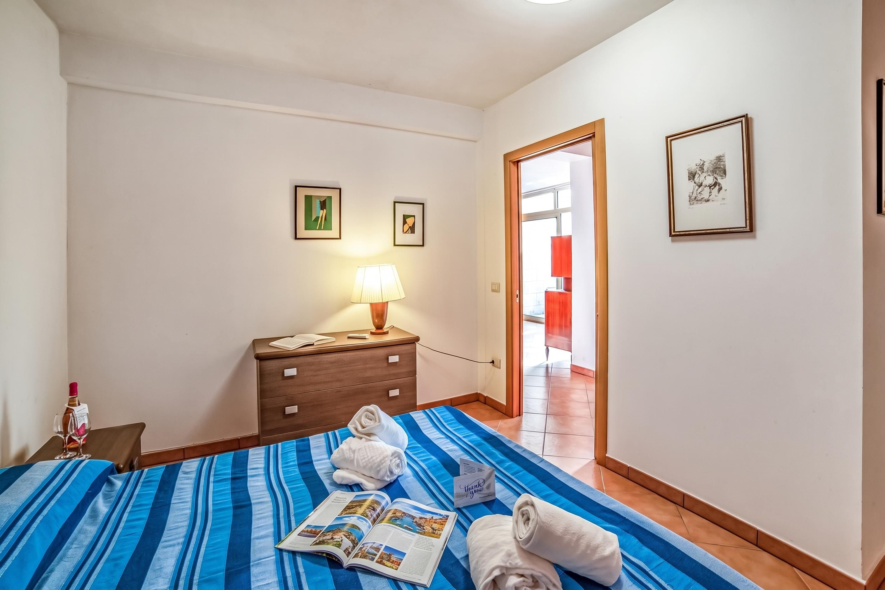 Een hotelkamer met een bed, een nachtkastje, een lamp en twee ingelijste foto’s aan de muur.
