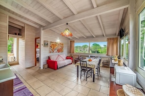 Una habitación amplia con zona de comedor, un sofá rojo, un ventanal grande y un ventilador de techo.