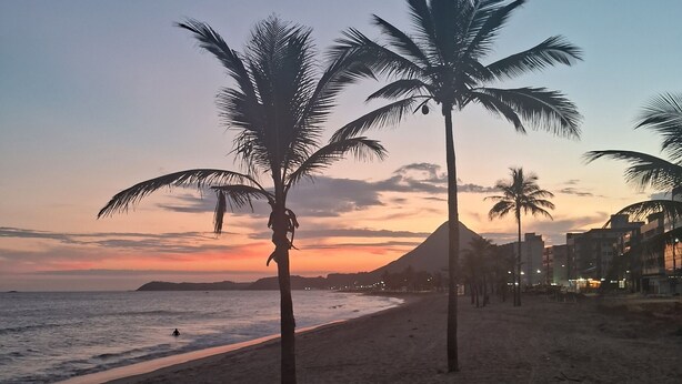 Ein Strand mit Palmen und einem Sonnenuntergang im Hintergrund.