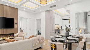 A modern living room with a fireplace, a dining area with a table set for four, and a kitchen in the background.