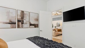 A bedroom with a bed, a gray blanket, and three abstract paintings on the wall.