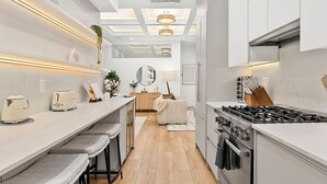 A modern kitchen with a central island, a dining area with bar stools, and a cozy seating area with a sofa and a lamp.