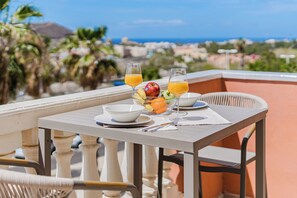Ein Balkon mit Tisch, einer Obstschale, zwei Orangensaftgläsern und einer Apfelschale.