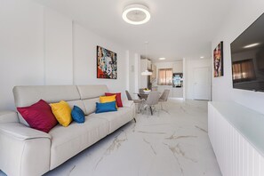 Ein modernes Wohnzimmer mit einer Couch, bunten Kissen, einem Essbereich und Kunstwerken an den Wänden.