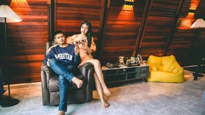 Una habitación con paneles de madera, un sofá de cuero negro, un sillón de peluche amarillo y una mesita con diversos objetos.