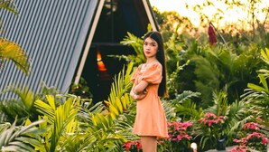 Una persona parada en un jardín con diversas plantas y un edificio al fondo.