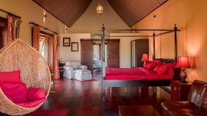 A spacious bedroom with a four-poster bed, a hanging chair, and a large window.