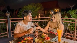 A couple dining at an outdoor table with a view of the night sky, surrounded by greenery and decorative lights.