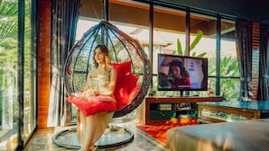 A woman sitting in a red chair in a room with a TV, large windows, and a patterned floor.