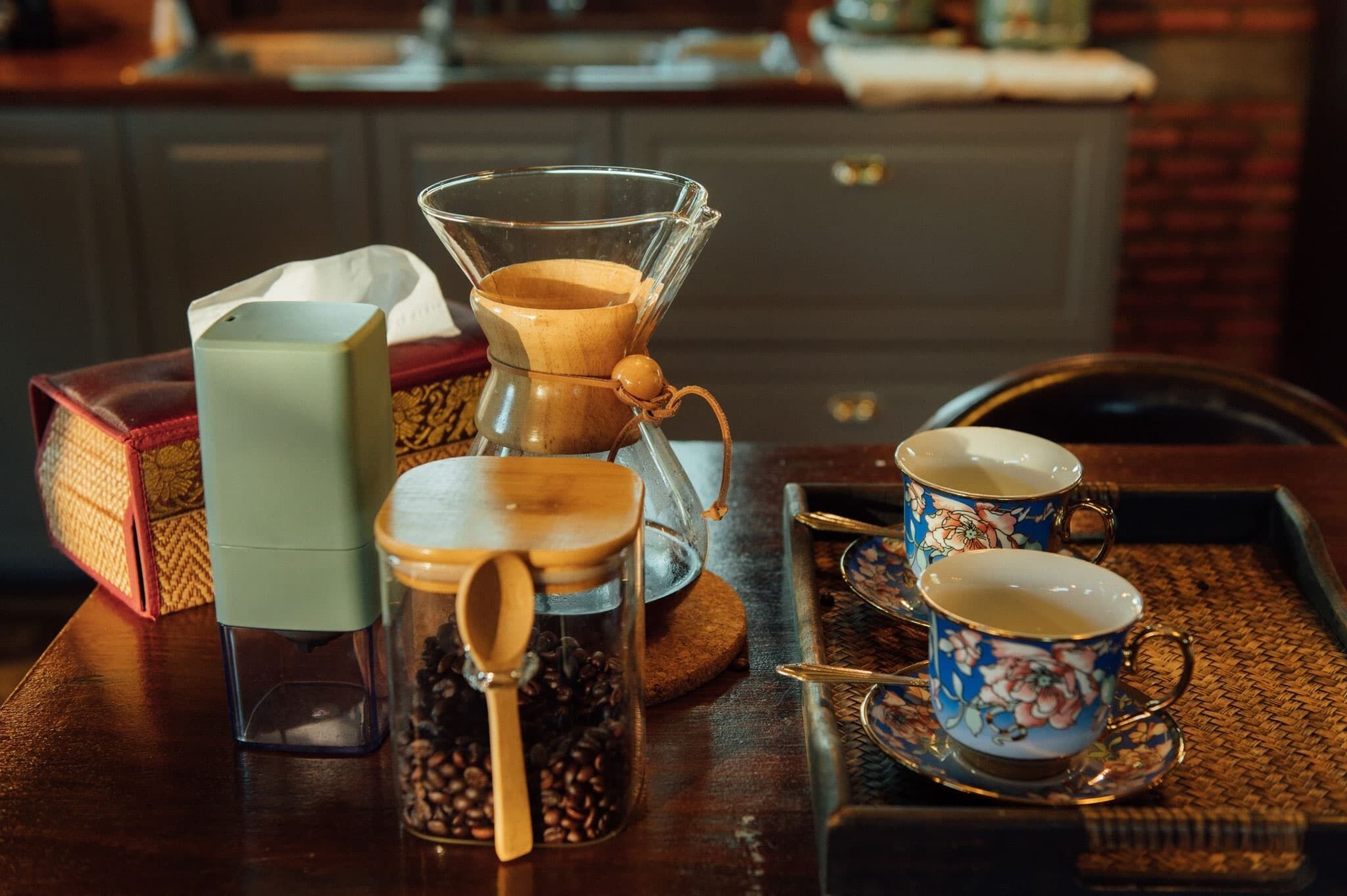 Uma cafeteira, um pote de grãos de café e duas xícaras sobre um tabuleiro.