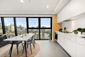 A modern kitchen with a city view, a dining area with a table and chairs, and a large window. - Waterfront 2BR Marina Tower, Rooftop Pool+Parking (Docklands)