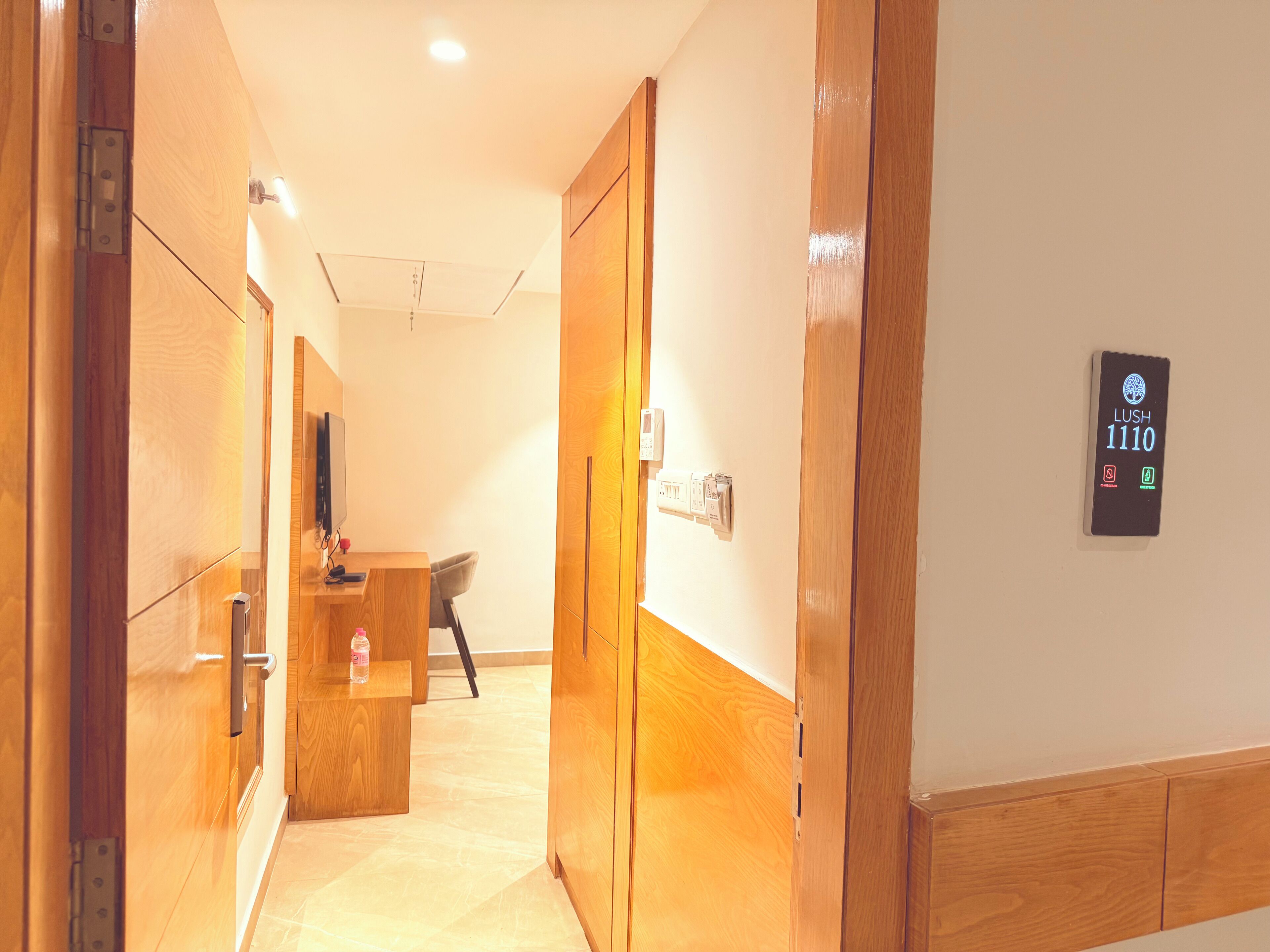 Een hotelhal met houten deuren, een receptiebalie en een apparaat op de muur dat kamer 1110 toont.
